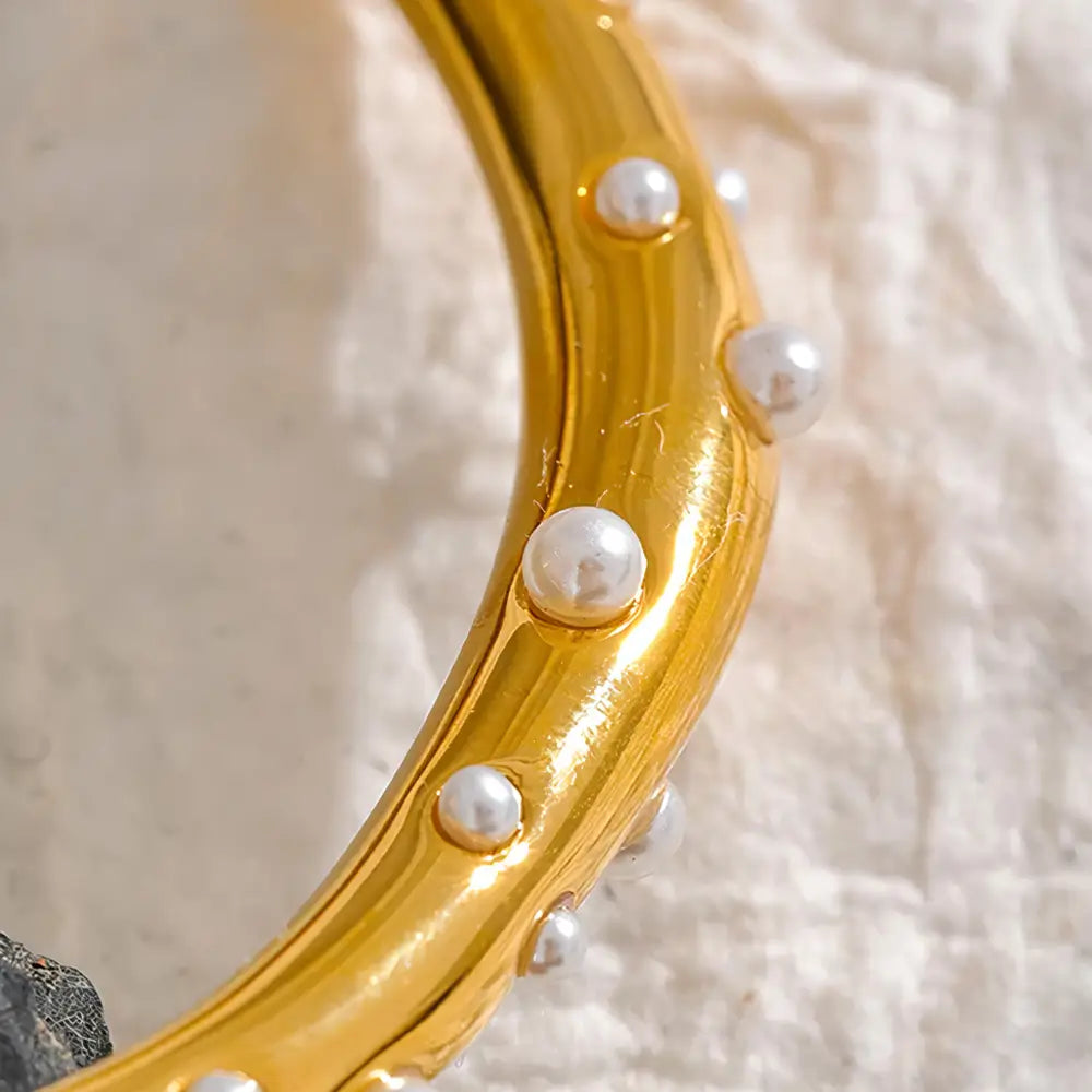 Bracelete Dourado Feminino cravejado com pérolas em fundo claro e elegante