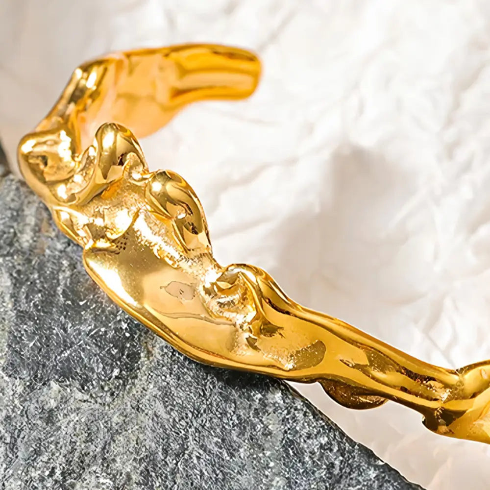 Bracelete Dourado Feminino rígido aberto irregular em cenário neutro com design marcante