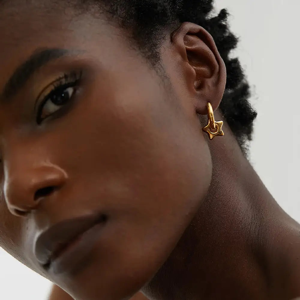 Mulher usando o Brinco Argola Feminino Dourado com Pingente de Estrela Estelari - Banhado a Ouro 18k
