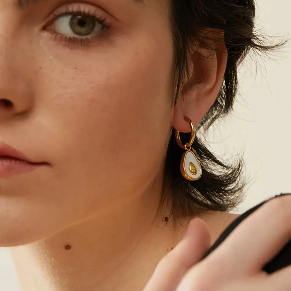 Foto de perto da Mulher usando o Brinco Feminino Argola Dourada com Pingente de Abacate de Concha Natural Amara - Banhado a Ouro 18k