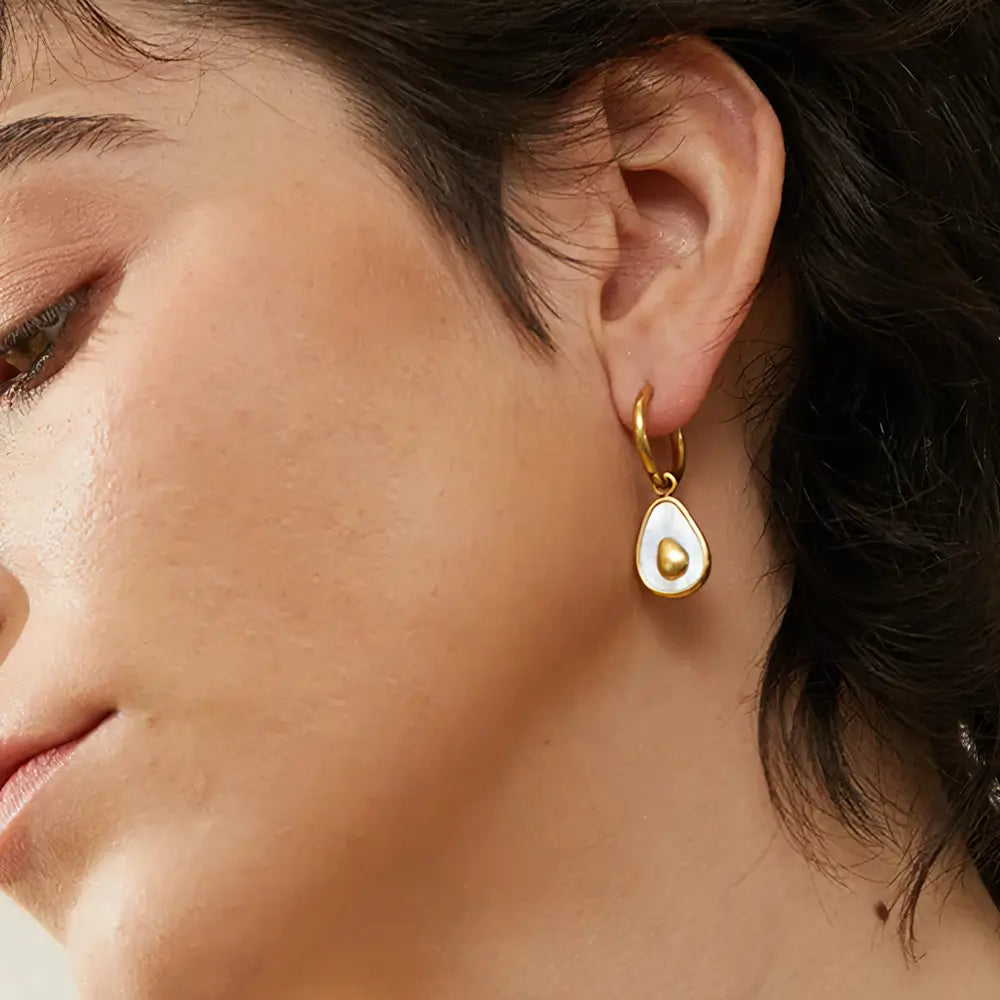 Foto lateral de perto da Mulher usando o Brinco Feminino Argola Dourada com Pingente de Abacate de Concha Natural Amara - Banhado a Ouro 18k