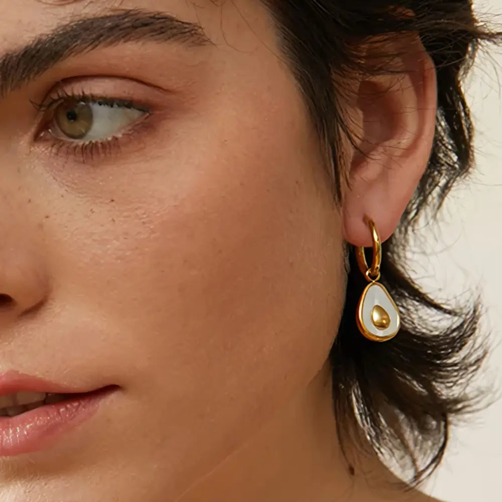 Foto frontal de perto da Mulher usando o Brinco Feminino Argola Dourada com Pingente de Abacate de Concha Natural Amara - Banhado a Ouro 18k
