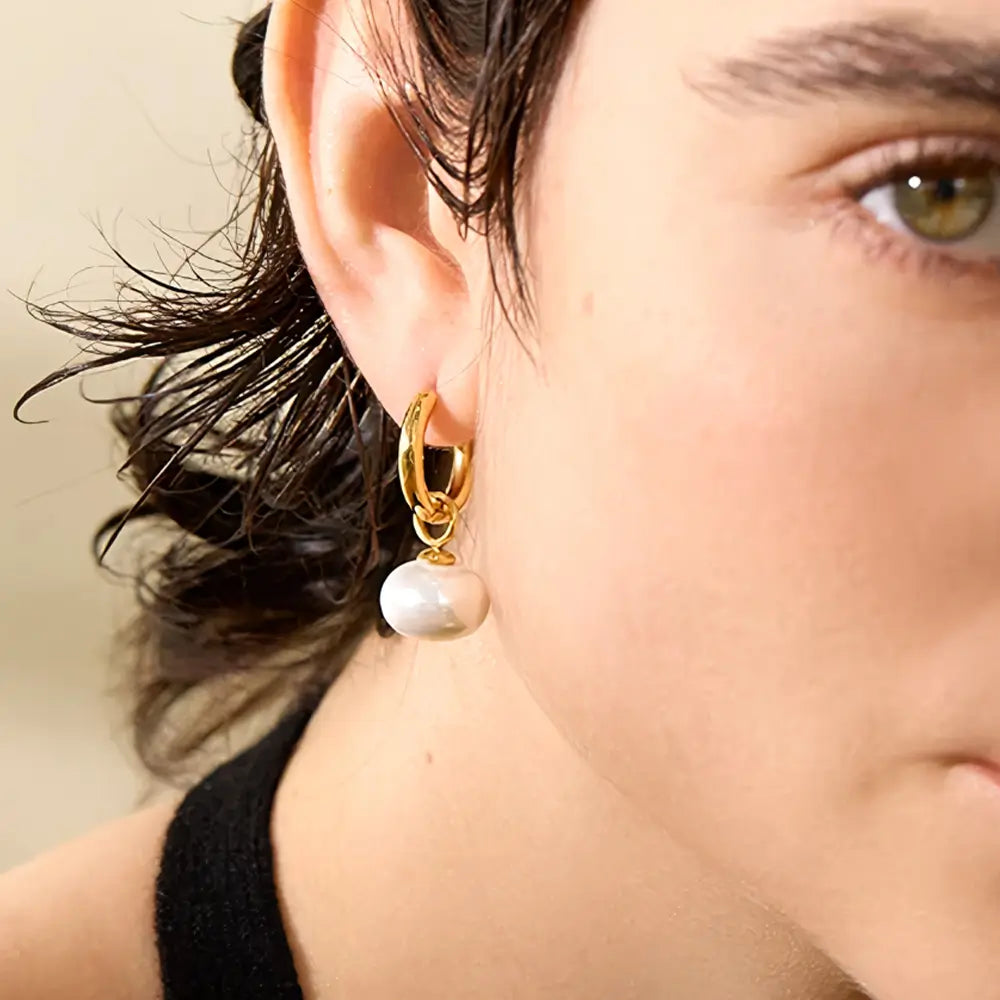 Foto lateral em detalhes, Mulher olhando usando o Brinco Feminino Argola Dourada com Pingente de Pérola Aurielle - Banhado a Ouro 18k