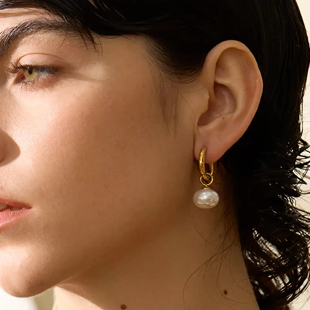 Mulher olhando para o lado usando o Brinco Feminino Argola Dourada com Pingente de Pérola Aurielle - Banhado a Ouro 18k