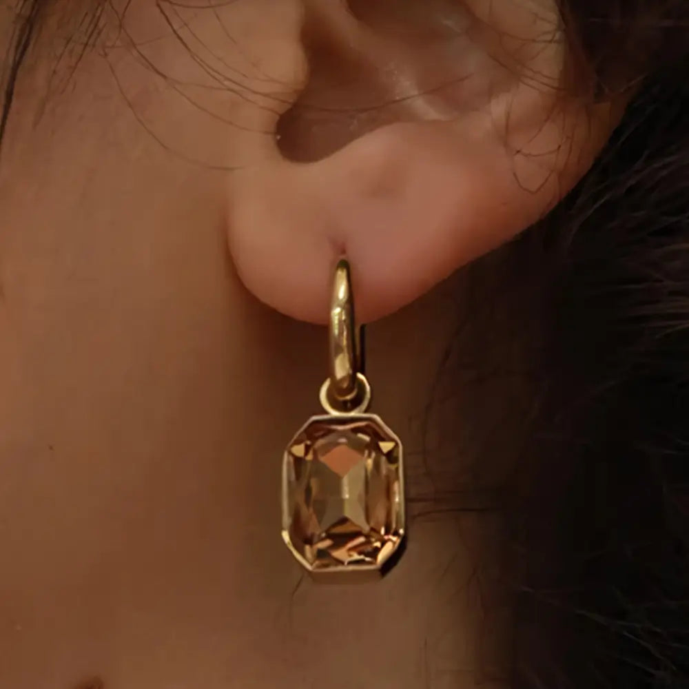 Foto de perto de uma Mulher usando o Brinco Feminino Argola Dourada com Pingente de Zircônia Corte Esmeralda Elina - Banhado a Ouro 18k