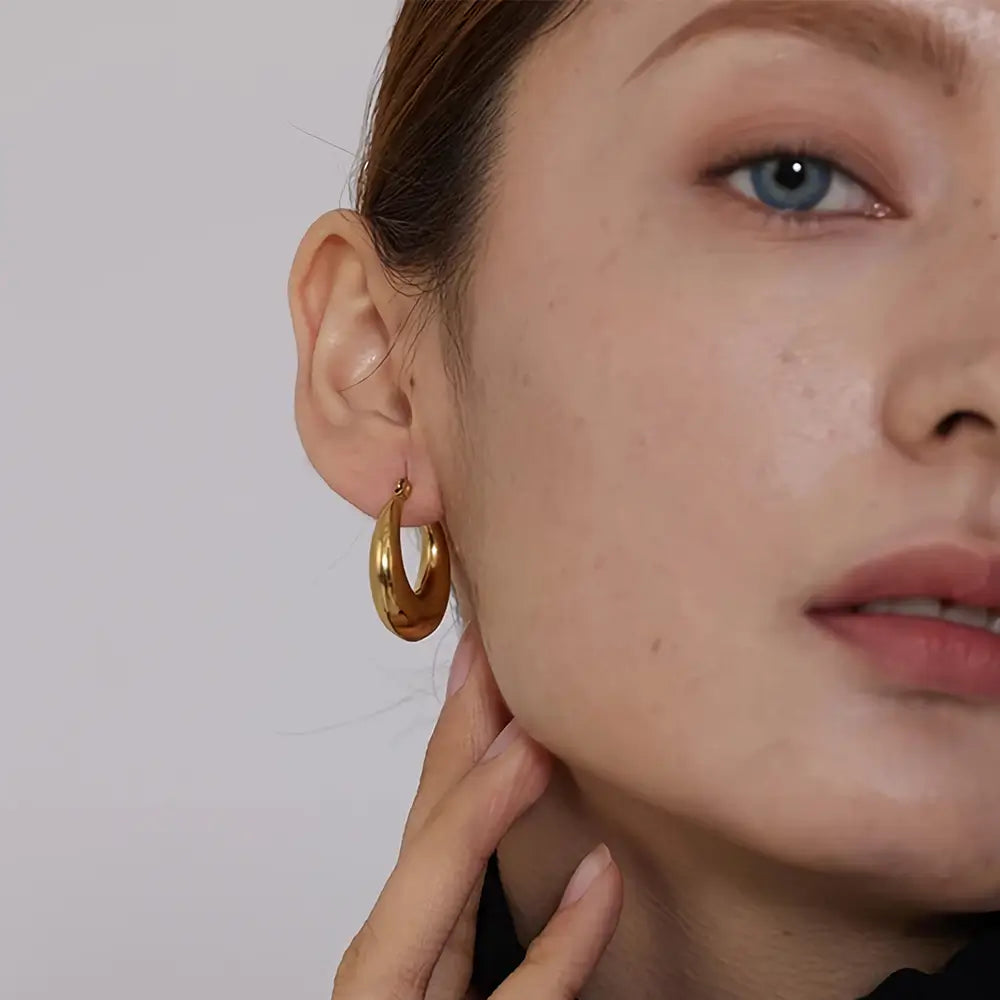 Foto frontal de uma Mulher usando o Brinco Feminino Argola Dourada Larga Meia Lua Selene - Banhado a Ouro 18k