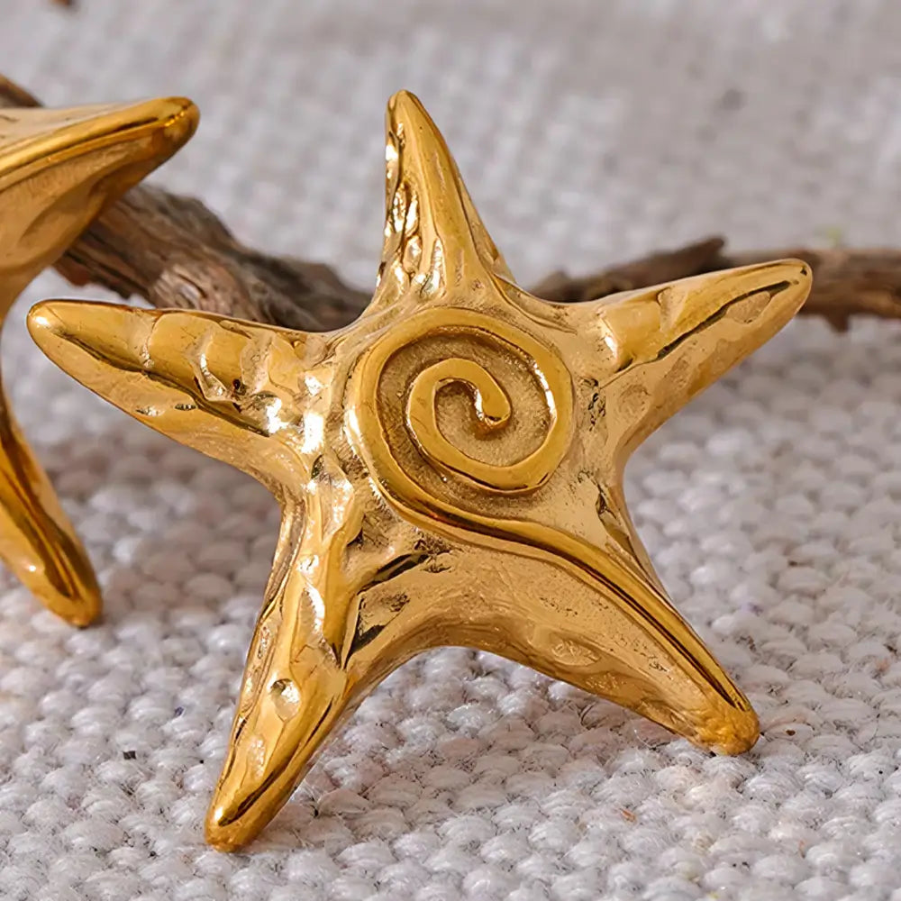 Brinco Feminino Dourado estrela do mar Maris com brilho suave em cenário neutro