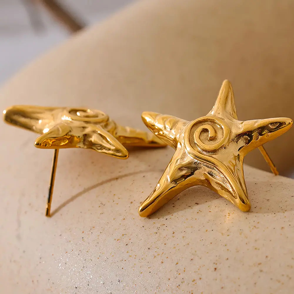 Brinco Feminino Dourado estrela do mar com formato delicado e luz difusa ao fundo