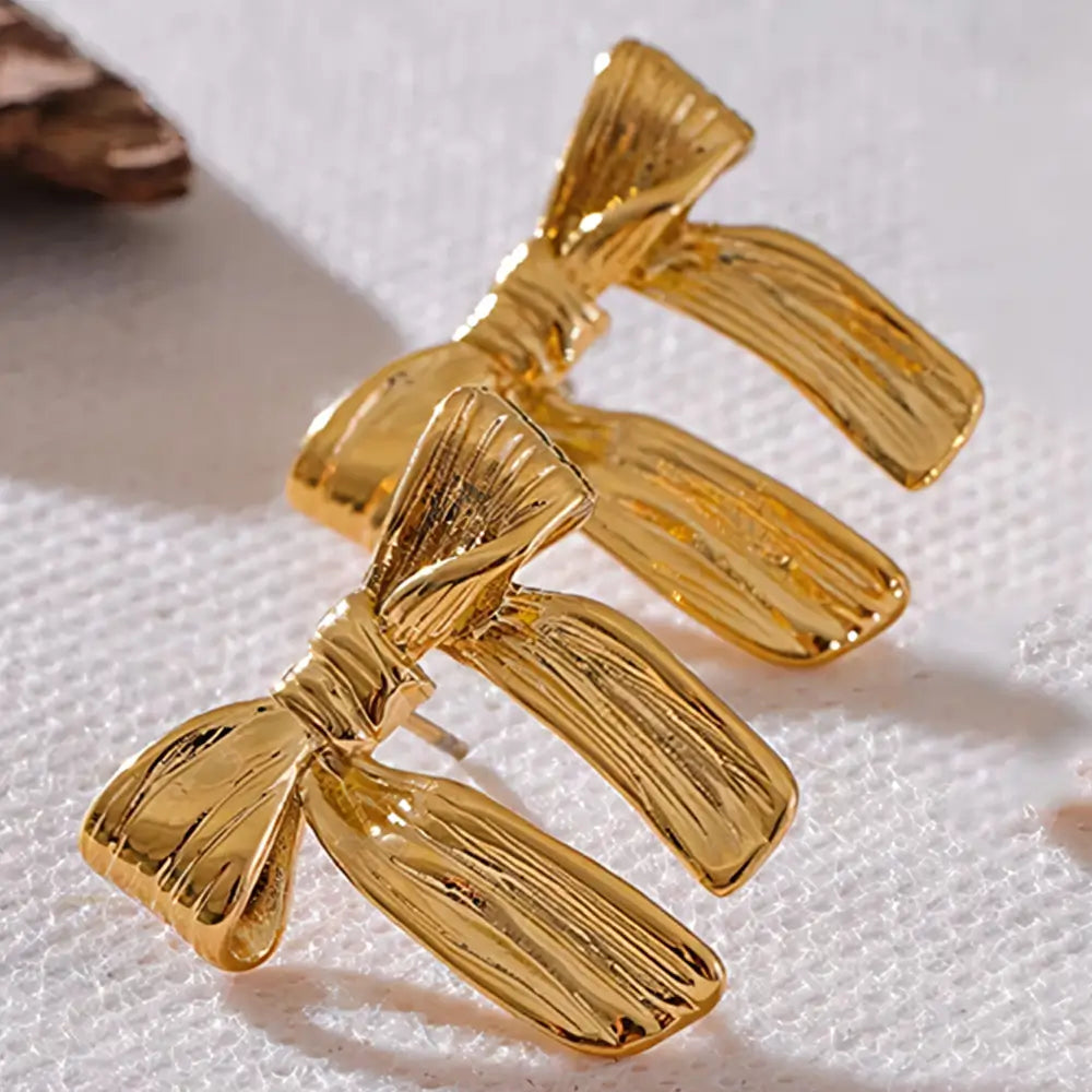 Brinco Feminino Dourado laço com textura rica e brilho suave em fundo neutro