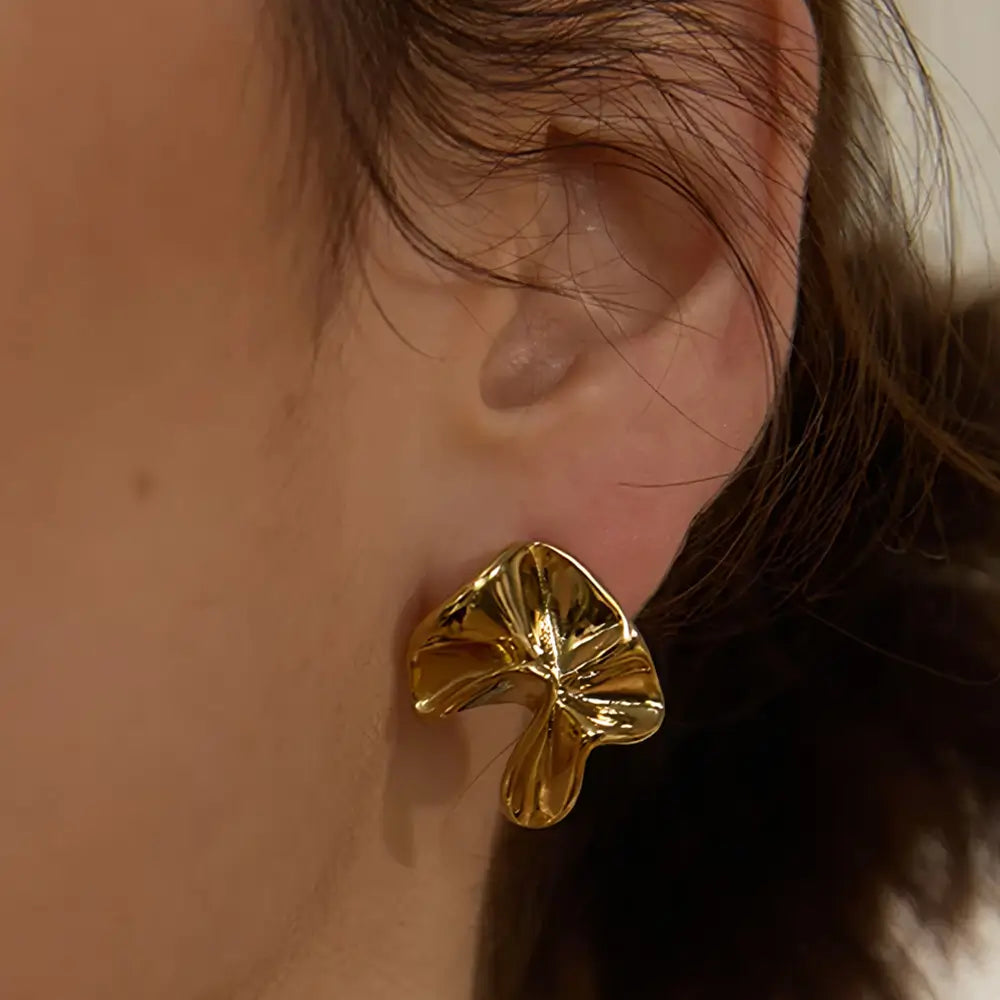 Brinco Feminino Dourado ondulado Maelle com textura orgânica e acabamento polido, foto de perto da orelha da modelo