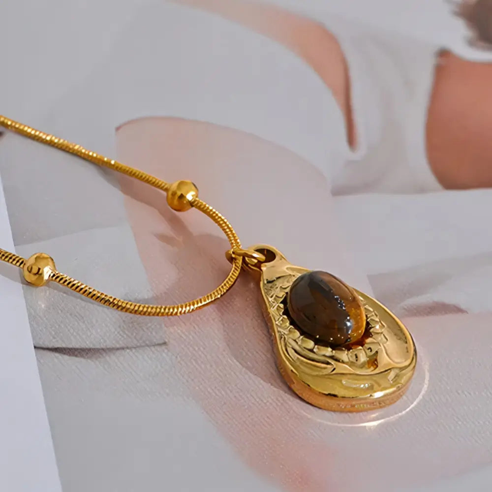 Colar Feminino Dourado de corrente rabo de rato com pingente e pedra tigre Cajúlia em fundo neutro com iluminação suave