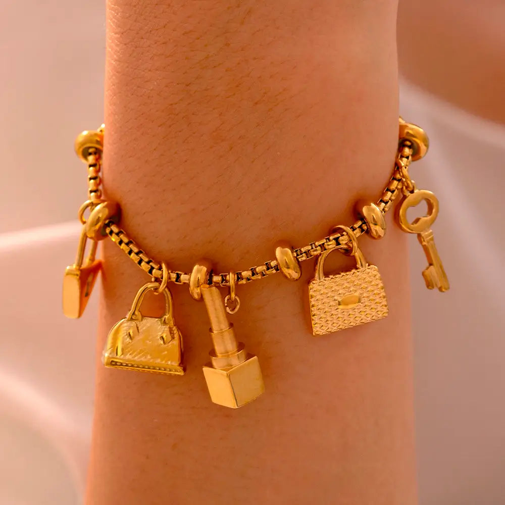 Pulseira Berloques em Aço Inox Dourada Feminina de Cadeado, Bolsa, Batom e Chave Luxelle - Banhada a Ouro 18k, foto de perto no braço