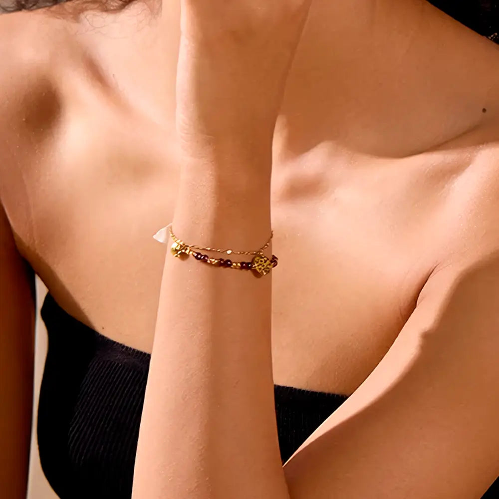 Foto do braço de uma Mulher usando a Pulseira Feminina Dourada Dupla de Pedras Naturais e Pingentes Aurélianne - Banhada a Ouro 18k