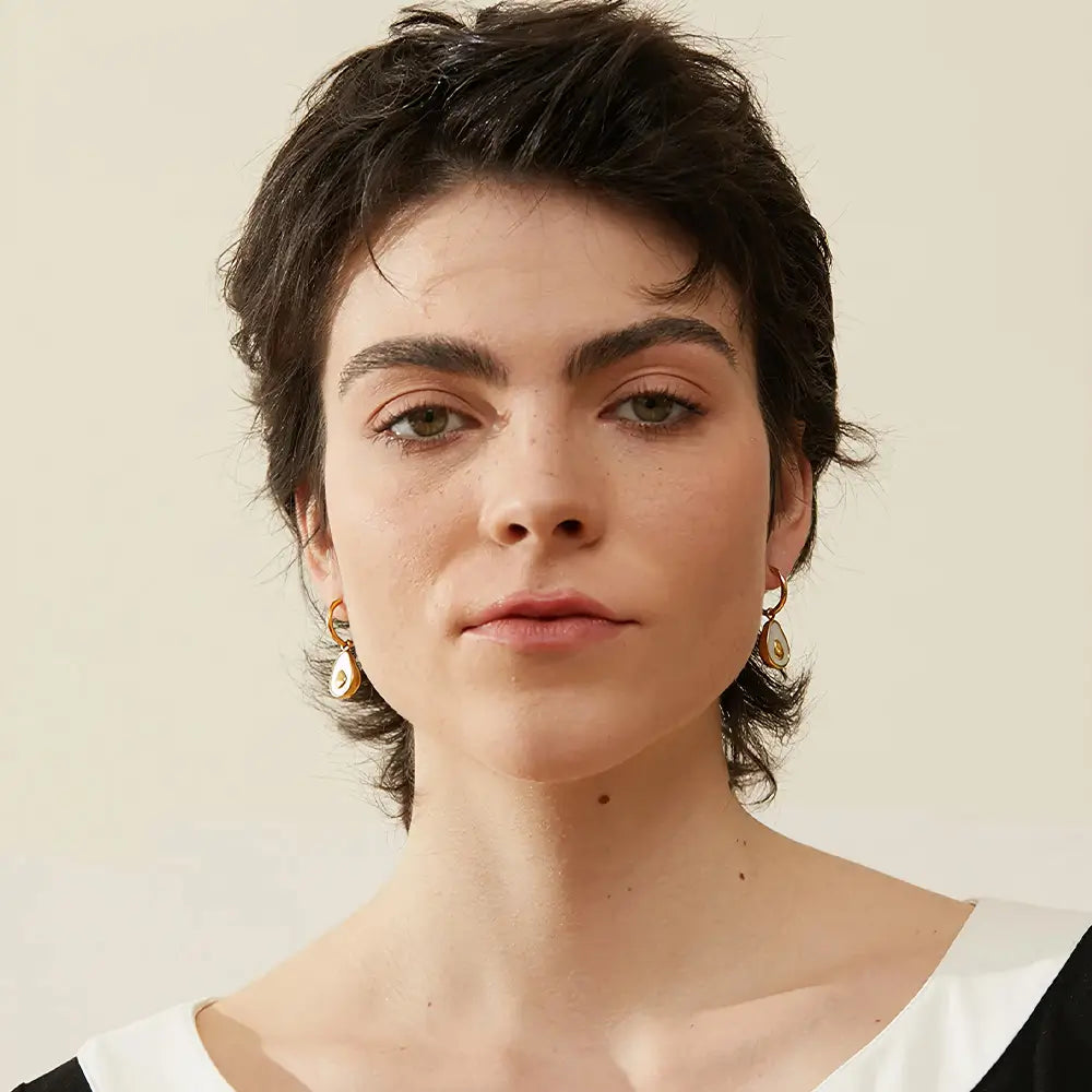 Mulher usando o Brinco Feminino Argola Dourada com Pingente de Abacate de Concha Natural Amara - Banhado a Ouro 18k