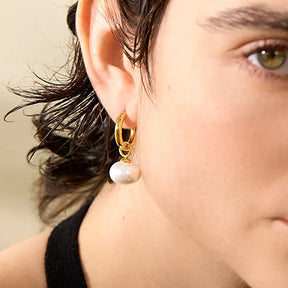 Foto lateral em detalhes, Mulher olhando usando o Brinco Feminino Argola Dourada com Pingente de Pérola Aurielle - Banhado a Ouro 18k