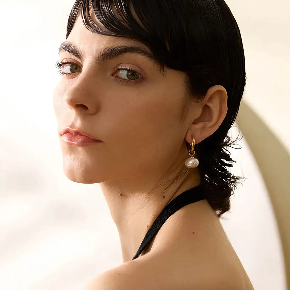 Foto lateral, Mulher olhando usando o Brinco Feminino Argola Dourada com Pingente de Pérola Aurielle - Banhado a Ouro 18k