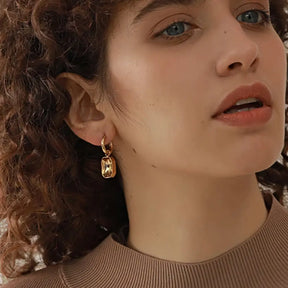 Foto frontal da Mulher usando o Brinco Feminino Argola Dourada com Pingente de Zircônia Corte Esmeralda Elina - Banhado a Ouro 18k