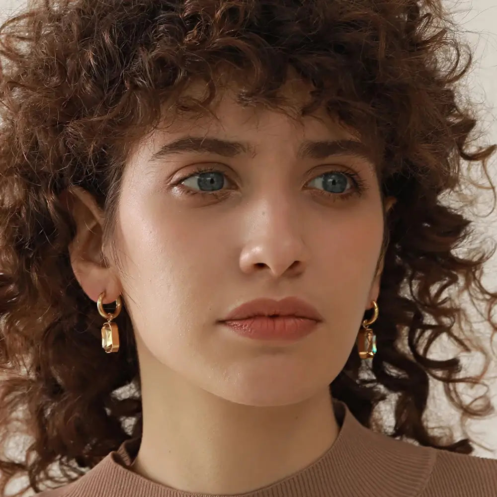Mulher usando o Brinco Feminino Argola Dourada com Pingente de Zircônia Corte Esmeralda Elina - Banhado a Ouro 18k