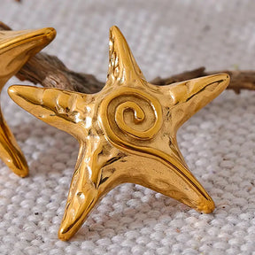 Brinco Feminino Dourado estrela do mar Maris com brilho suave em cenário neutro