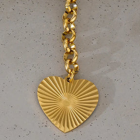 Colar Feminino Dourado elo português com acabamento brilhante e coração dourado em cenário minimalista
